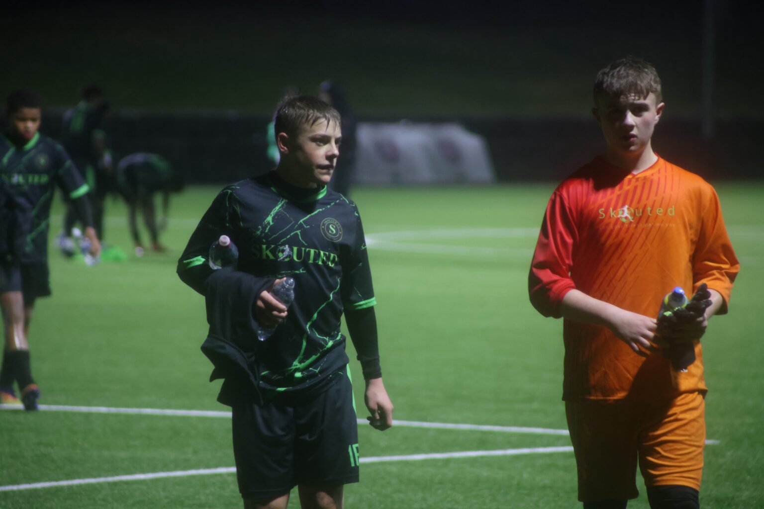 Skouted players walking off a floodlit pitch after a match